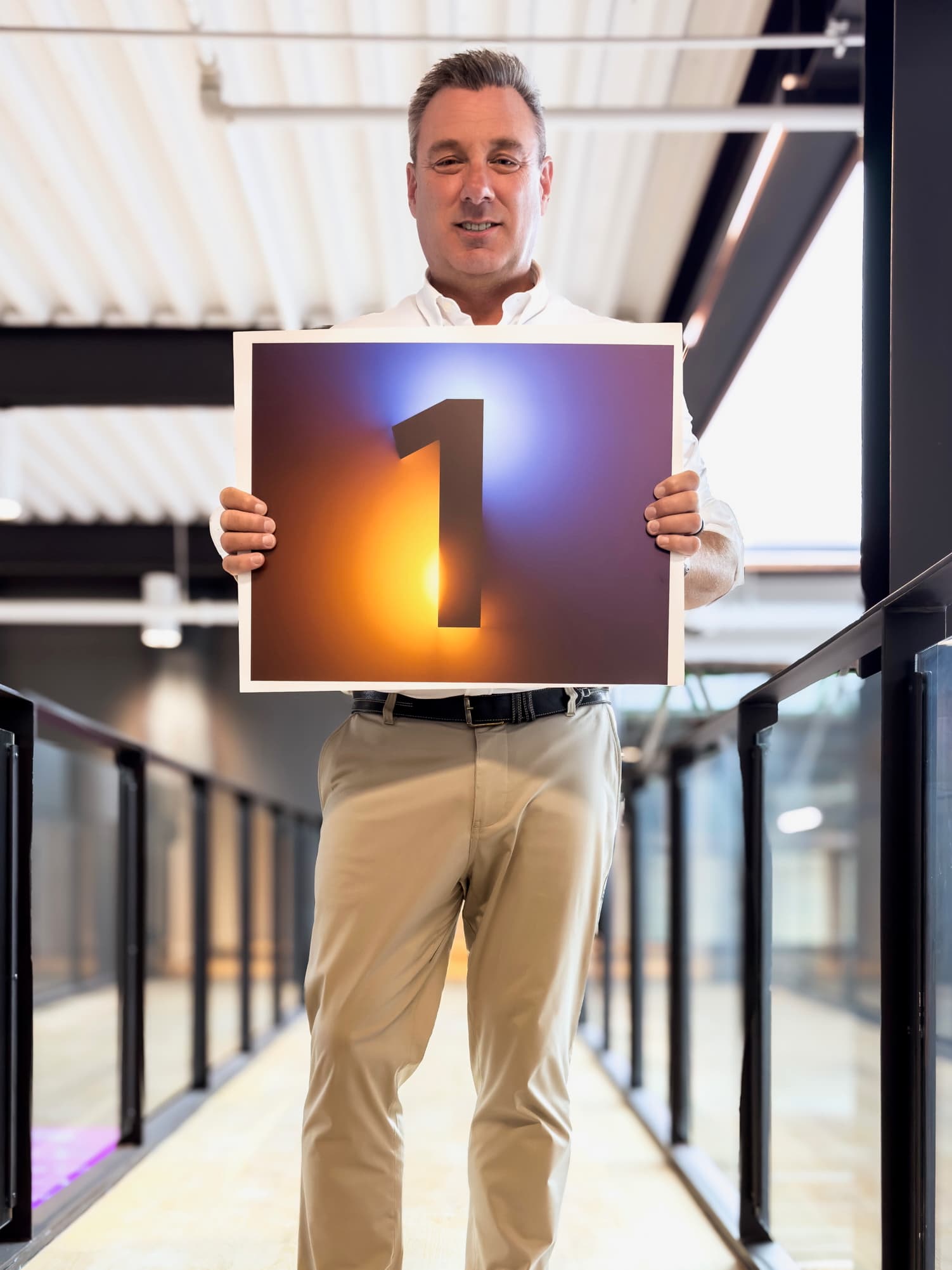 Smiling man in a white shirt holds a large sign featuring a glowing number one.