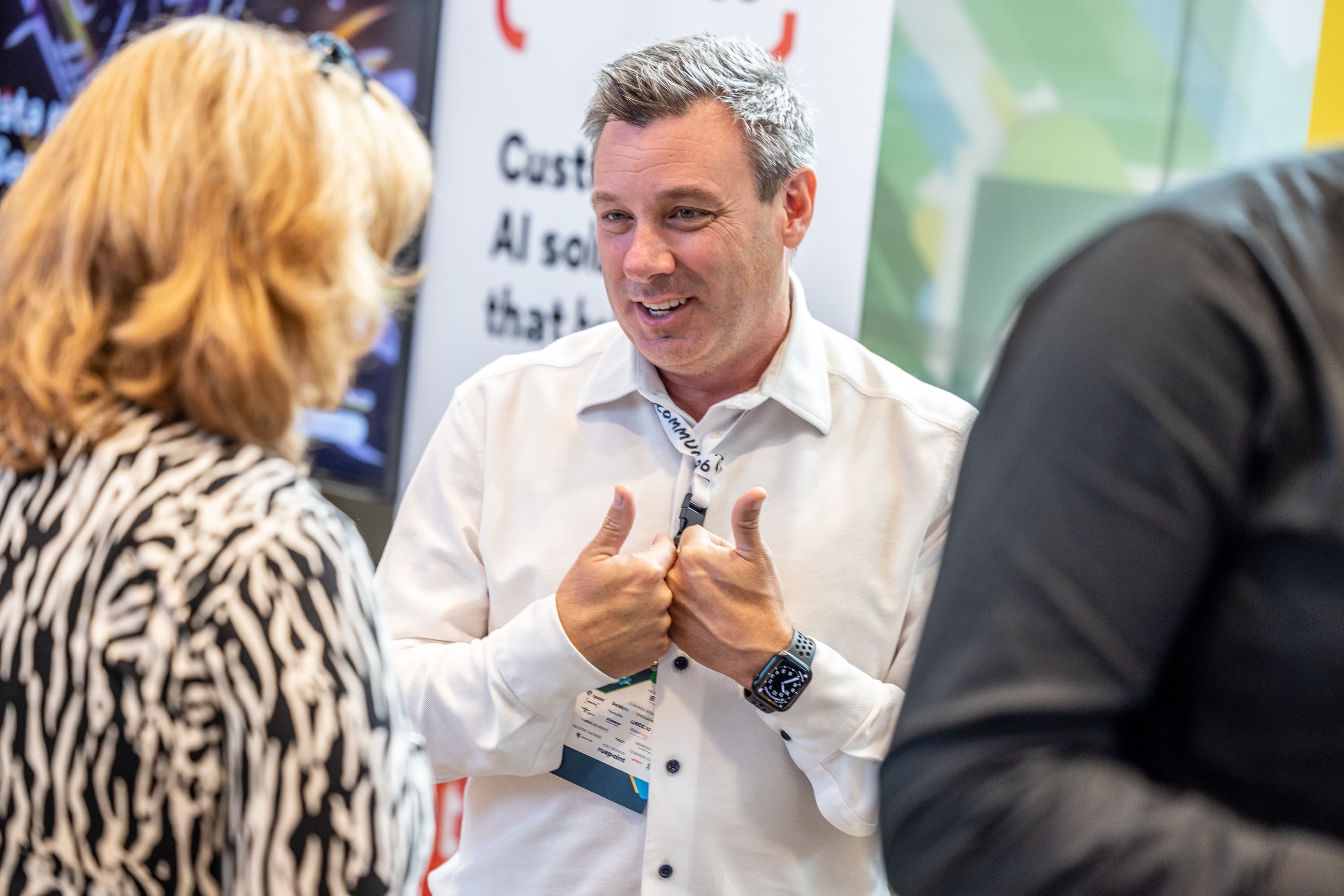 Smiling man in a white shirt gives two thumbs up while talking to a woman.