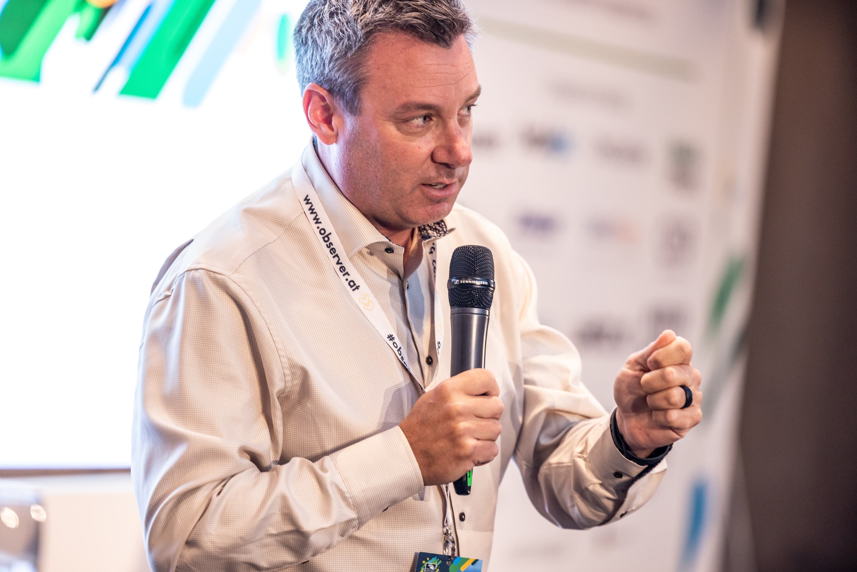 Man in a light shirt speaking into a microphone and gesturing with a clenched fist.