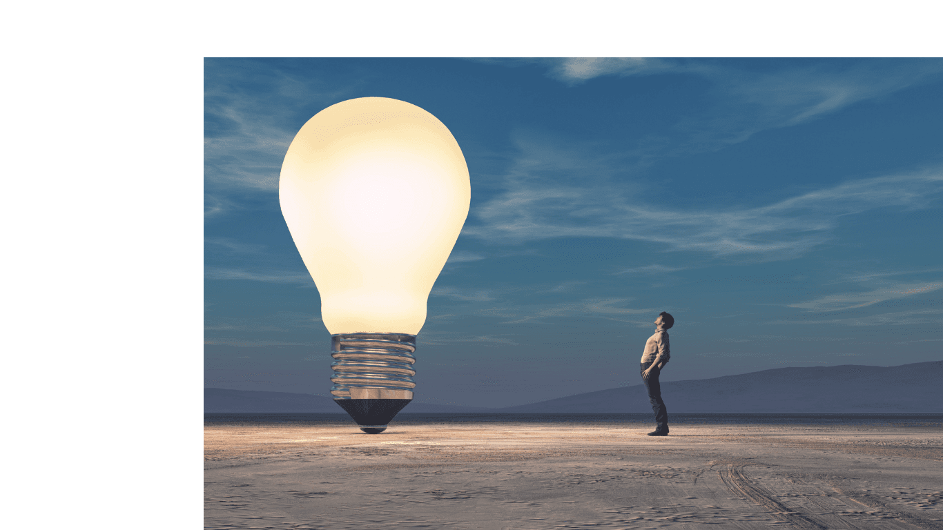 Man gazes up at a massive, glowing light bulb in a vast desert landscape.