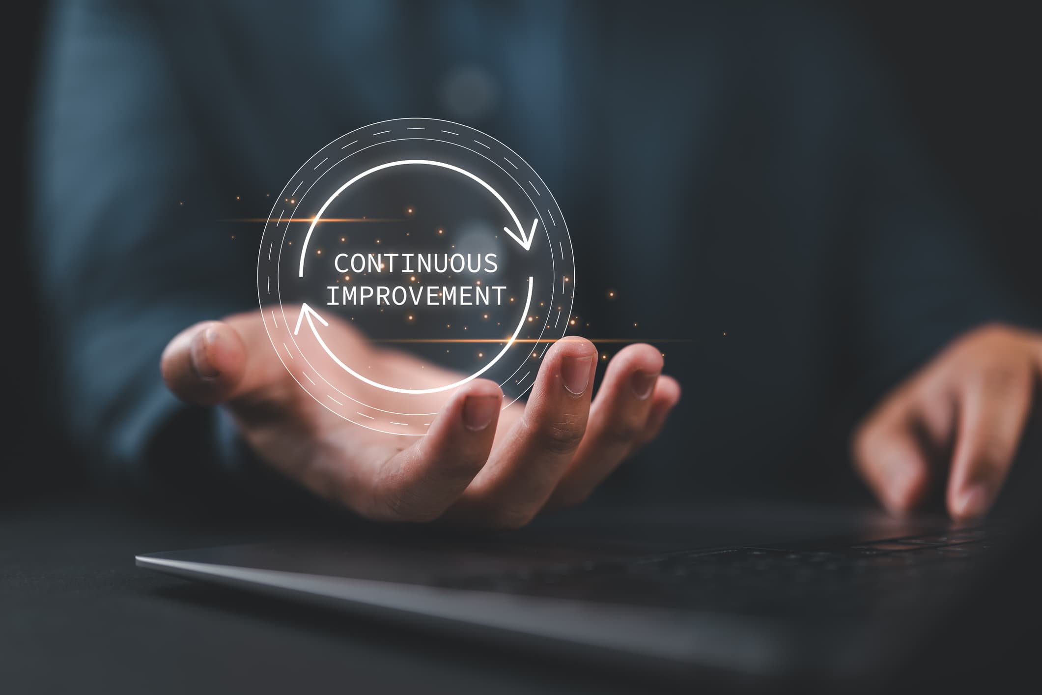 Glowing circular arrows and 'Continuous Improvement' text floating above a person's open hand.