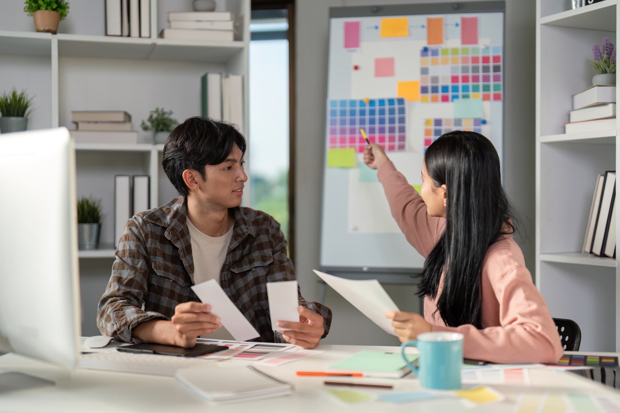 Two creative professionals discuss color palettes and design ideas in a bright, modern office.