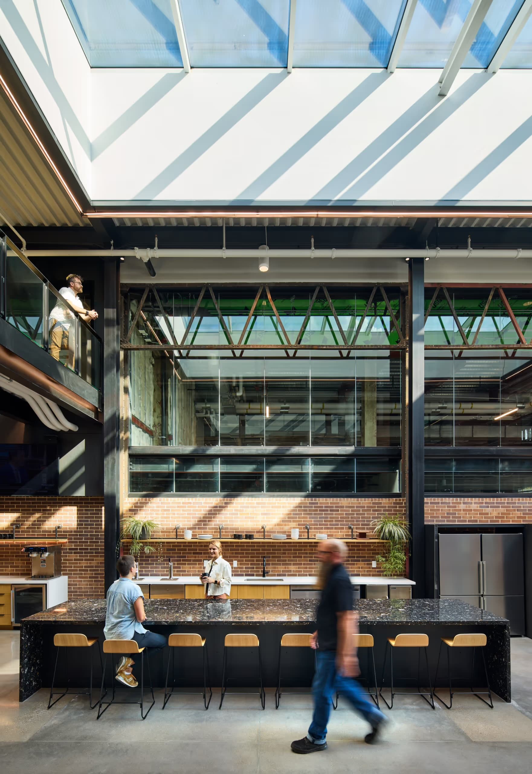 Modern industrial office with a large skylight, brick walls, and people at a granite bar.
