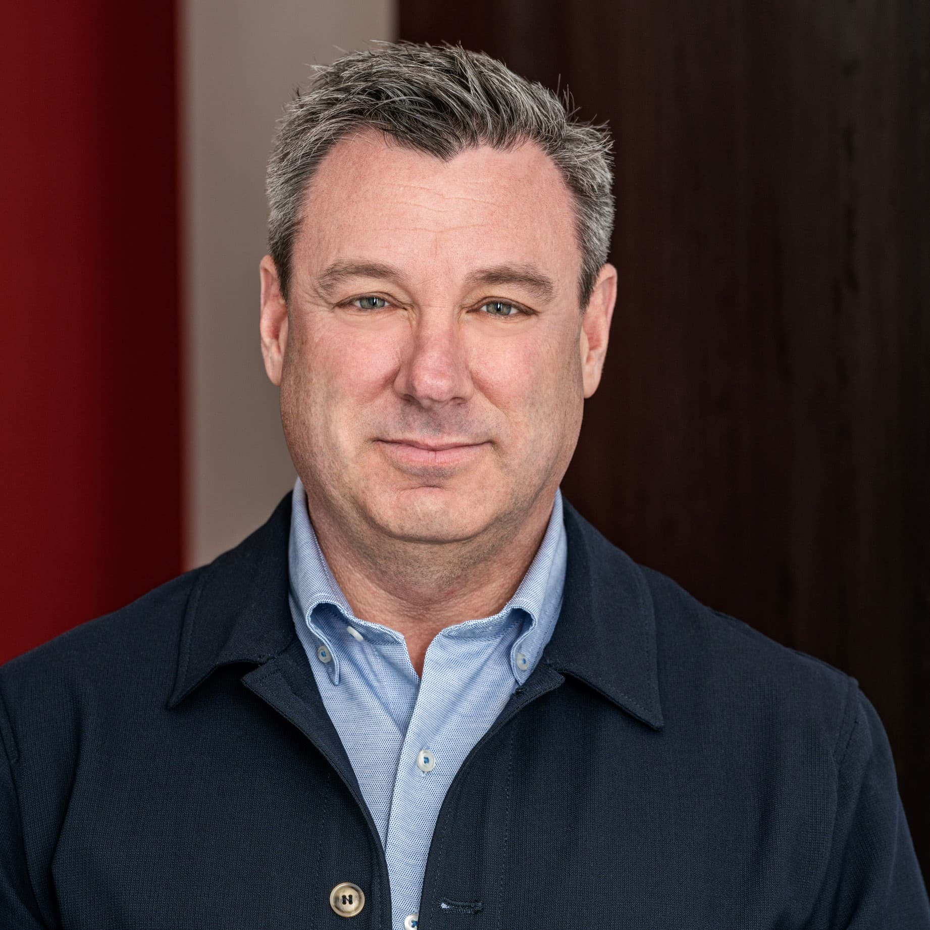 Middle-aged man with salt-and-pepper hair, wearing a light blue shirt and navy blue jacket.